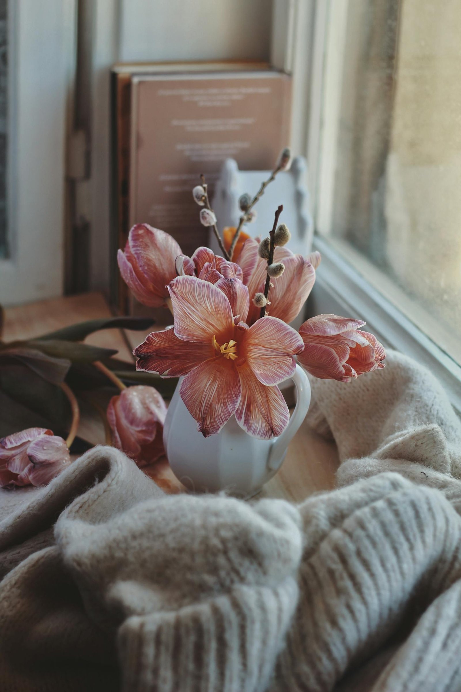 A vase of pink flowers with a cozy sweater beside a window, creating a serene spring decor.