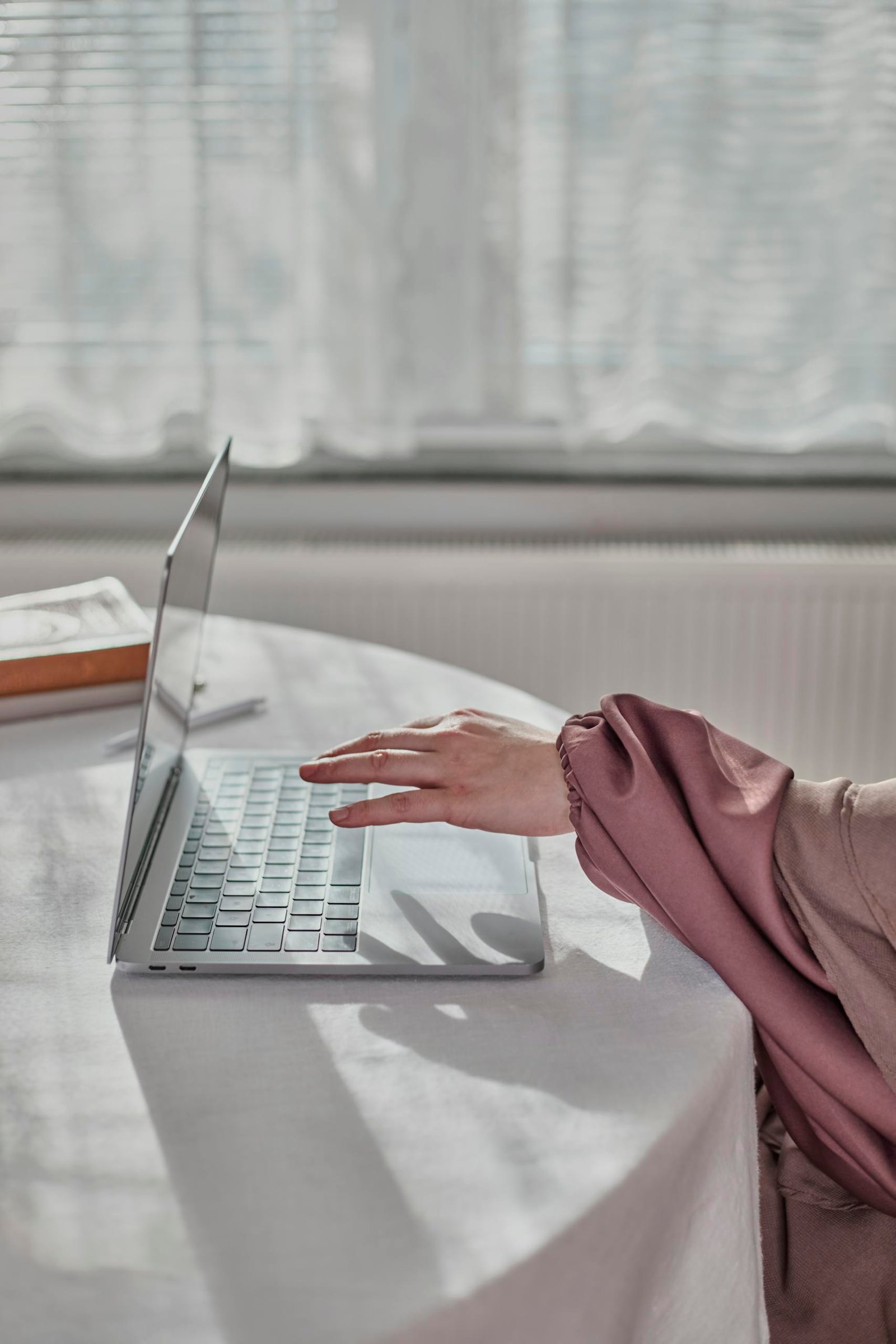 A hand in an elegant sleeve uses a laptop indoors with soft natural light.
